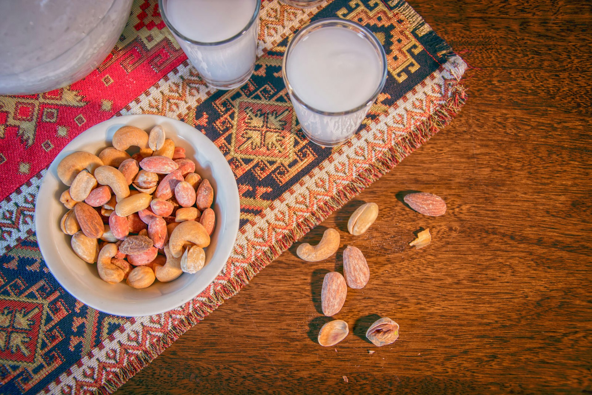 Two glasses of arak and a plate of nuts on a tabletop 