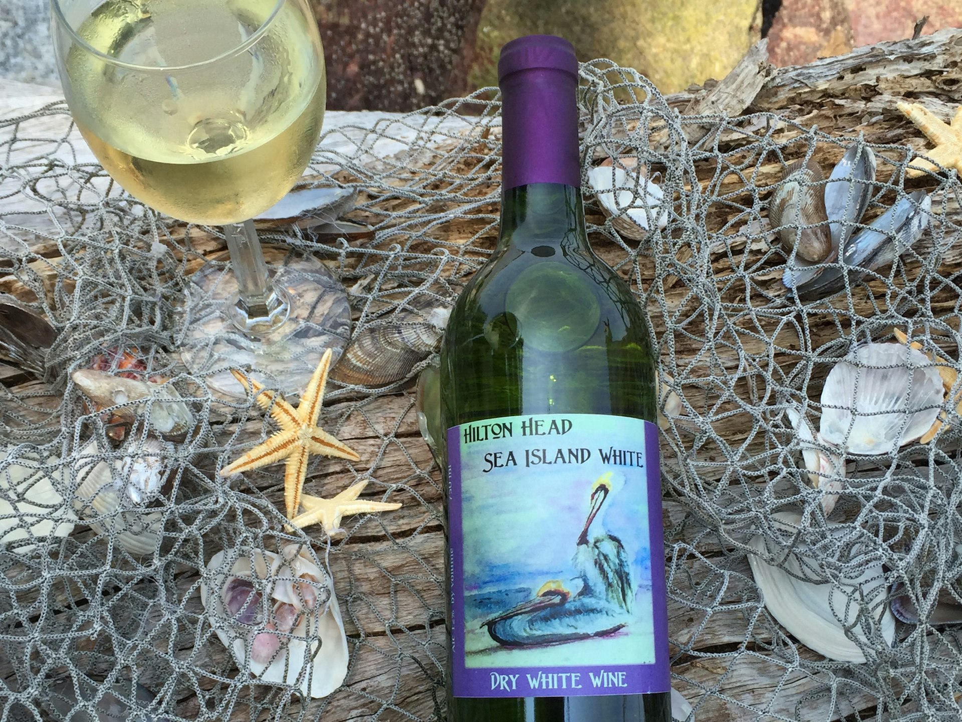 A glass of Island Winery wine and a bottle in a nest of sea shells and star fish