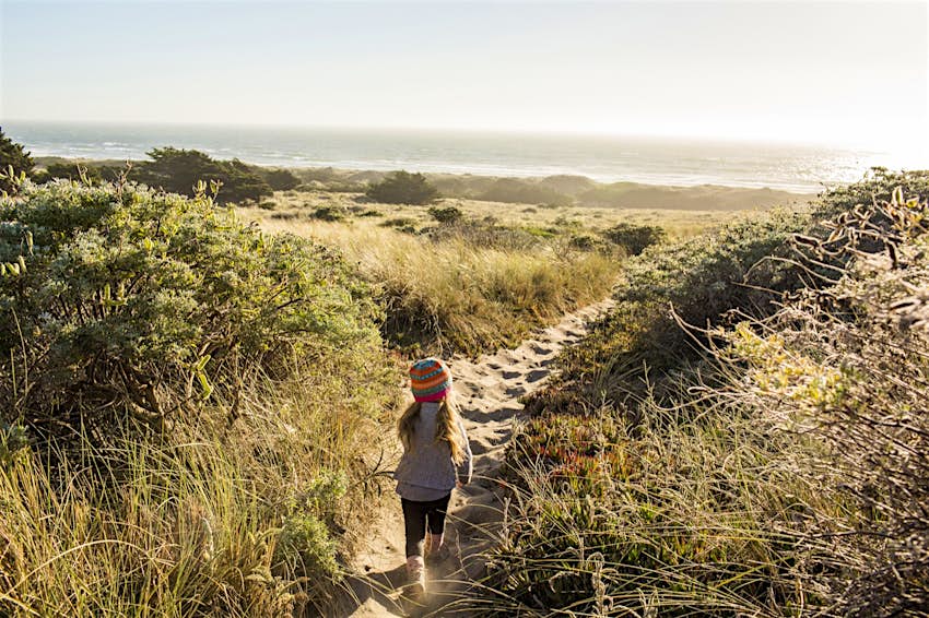 A small girl runs down a sandy path to the beach near Jenner California