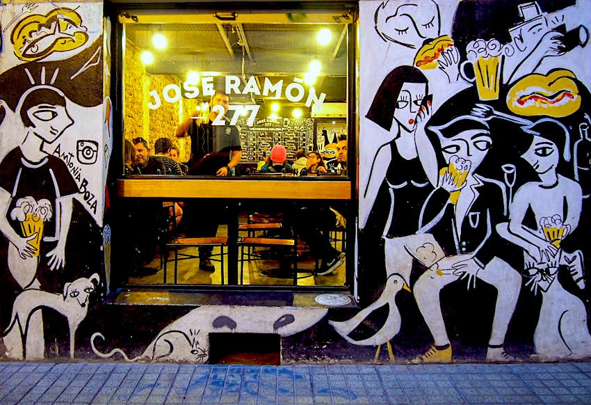 The exterior of restaurant Jose Ramon; one window is surrounded by a wall of black and white murals of people eating food. Santiago, Chile.