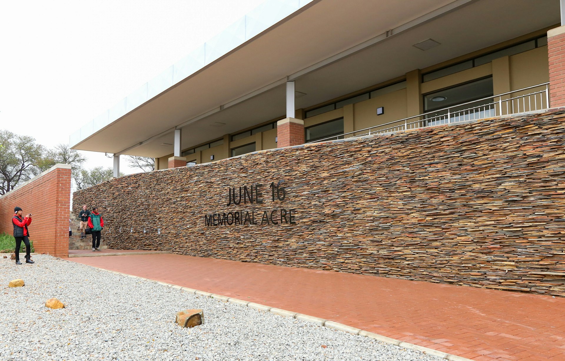Johannesburg June - A brick walkway passes beneath a stone wall with raised black letters spelling June 16 Memorial Acre; a building stands behind