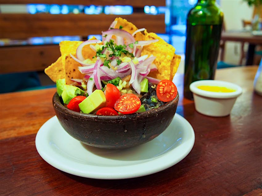 A stone bowl sits full of vegetarian ceviche containing avocado, tomatoes, kelp, onion and corn chips at El Huerto. Santiago, Chile.