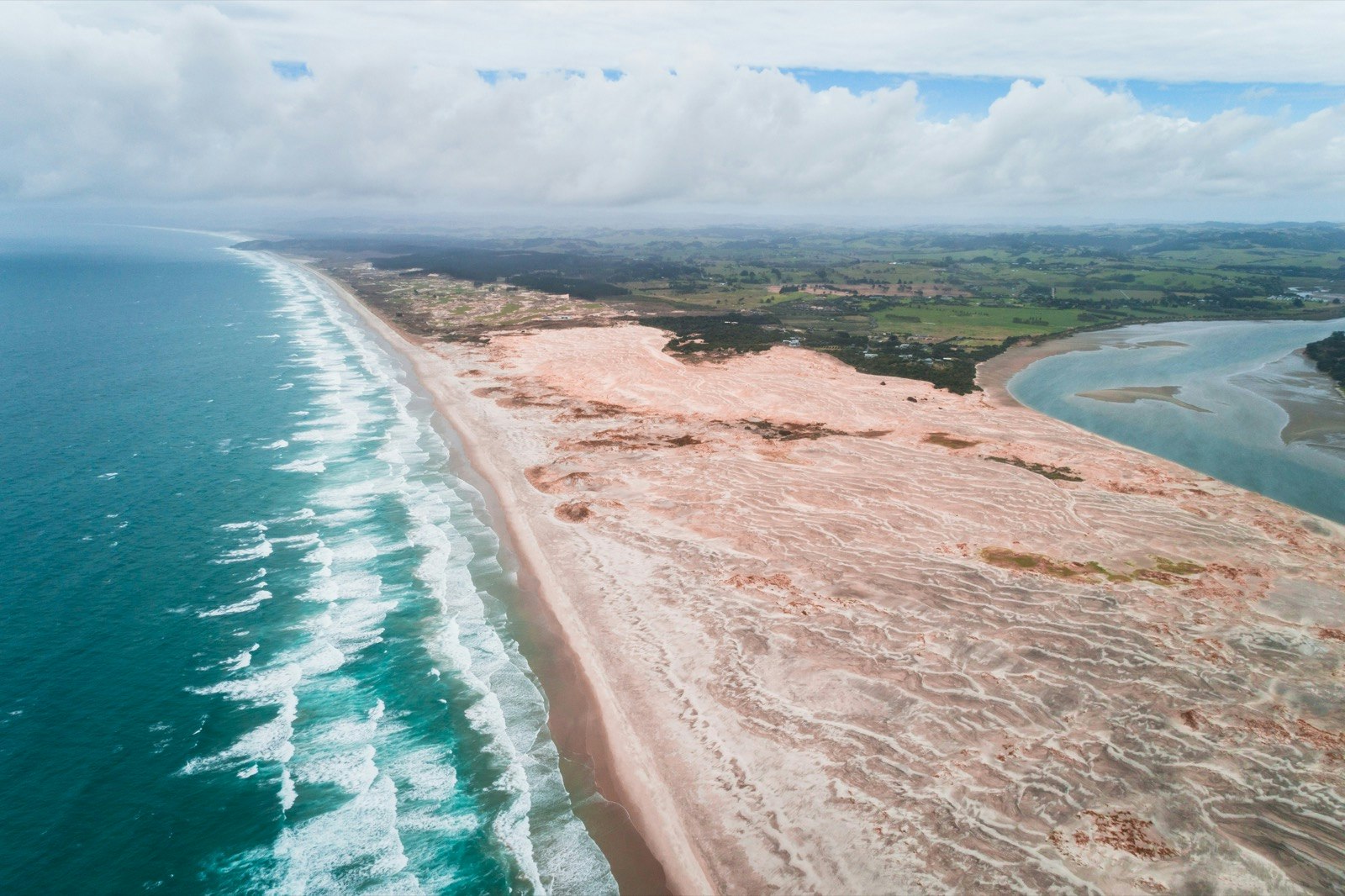Aerial view of Mangawhai heads, North Island, New Zealand; lines of white waves build as they approach the azure shallows before crashing on the pinkish sands
