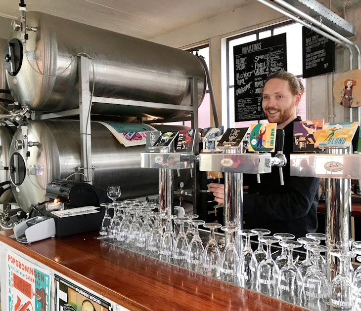 A man pulls a pint behind the bar at Brouwerij Martinus. There are craft brews on tap and large silver stills tucked next to the bar © Sara van Geloven/Lonely Planet