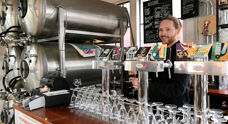 A man pulls a pint behind the bar at Brouwerij Martinus. There are craft brews on tap and large silver stills tucked next to the bar © Sara van Geloven/Lonely Planet