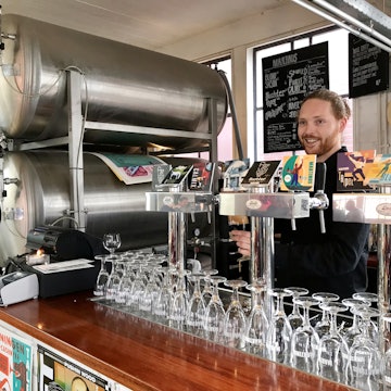 A man pulls a pint behind the bar at Brouwerij Martinus. There are craft brews on tap and large silver stills tucked next to the bar © Sara van Geloven/Lonely Planet