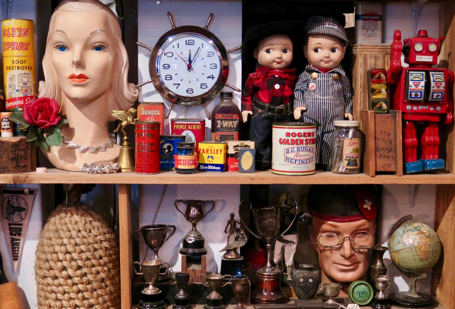 An array of kitschy items, including dolls and a ship's steering wheel clock are seen on shelves in a vintage store