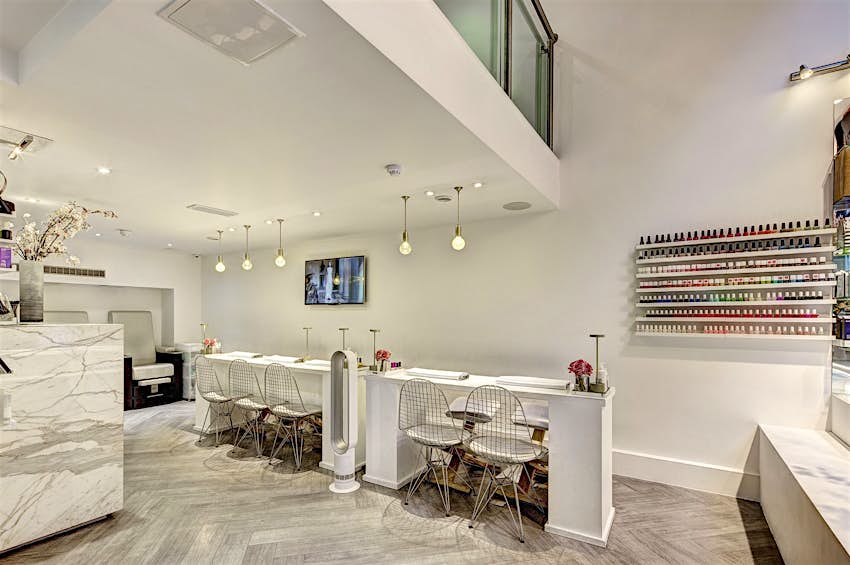 Image shows the salon with hundreds of nail polishes lining the walls and trendy iron seats in front of the nail stations