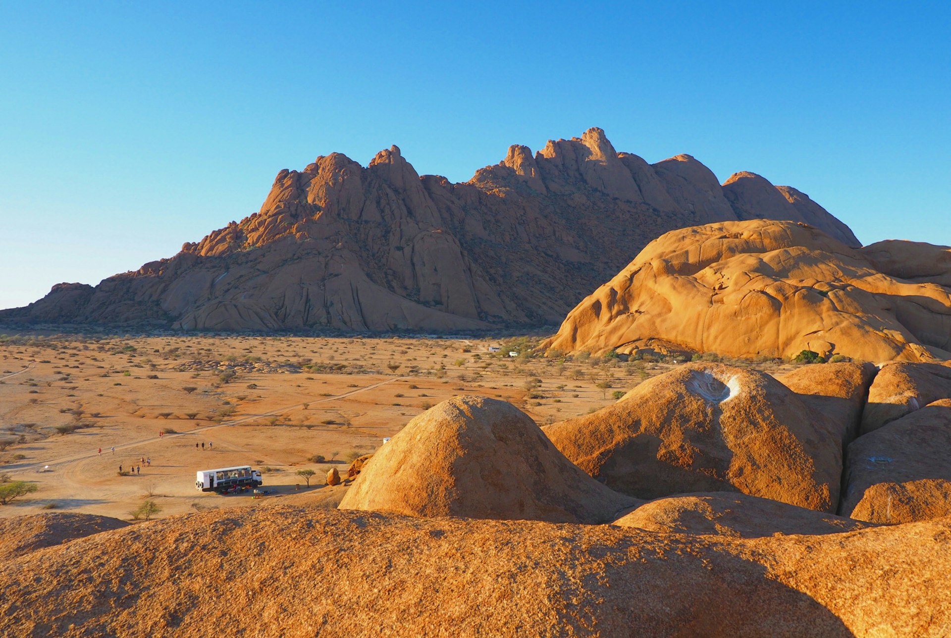 A large overland truck looks much like a toy brick as it sits on the red Namibian soil surrounded by massive, bulbous rock monoliths at Spitzkoppe @ Sarah Reid / Lonely Planet