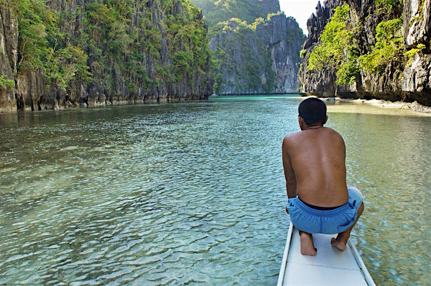 Palawan travel - EL NIDO, PALAWAN, PHILIPPINES - A canoe is heading into a hidden lagoon in Palawan archipelago. A man crouches near the top of the canoe wearing blue swimming shorts (Photo by Jonas Gratzer/LightRocket via Getty Images)