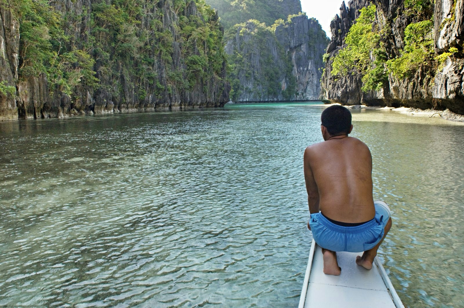 Palawan travel - EL NIDO, PALAWAN, PHILIPPINES - A canoe is heading into a hidden lagoon in Palawan archipelago. A man crouches near the top of the canoe wearing blue swimming shorts (Photo by Jonas Gratzer/LightRocket via Getty Images)