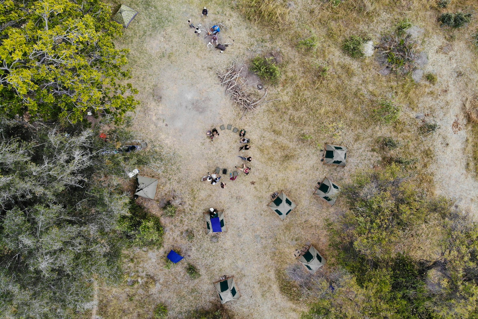 An aerial picture taken from a drone, looking down on a collection of dome tents and campers sitting on folding camp chairs in a semi-circle; a little distance away another group cooks dinner over a campfire @ Sarah Reid / Lonely Planet