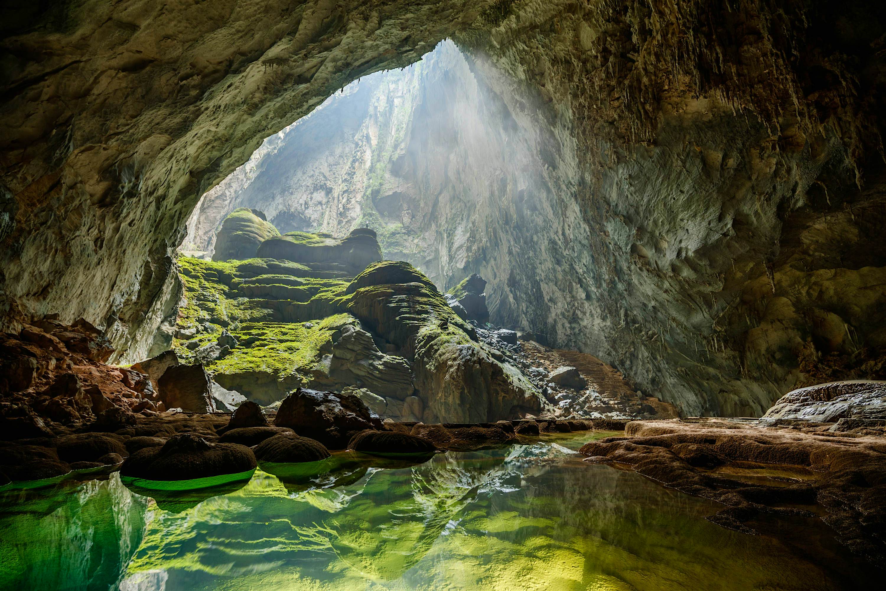 Sunlight shines down through an opening in the cave into a clear green pool of water