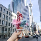 Tufts of pink and blue cotten candy poke out of an ice cream cone held in front of the CN tower in Toronto