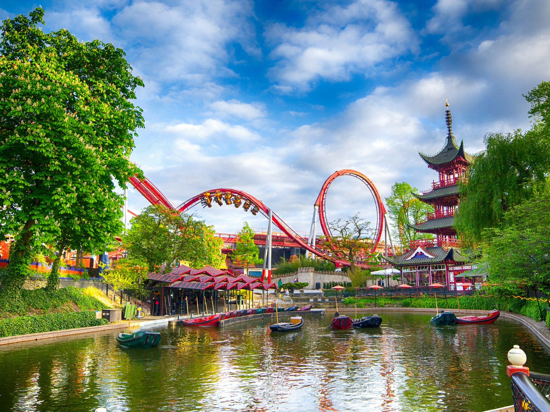 Disney alternatives - Colourful Tivoli Gardens in Copenhagen. A red rollercoaster twists over the park's lake which has small green and red boats floating on it