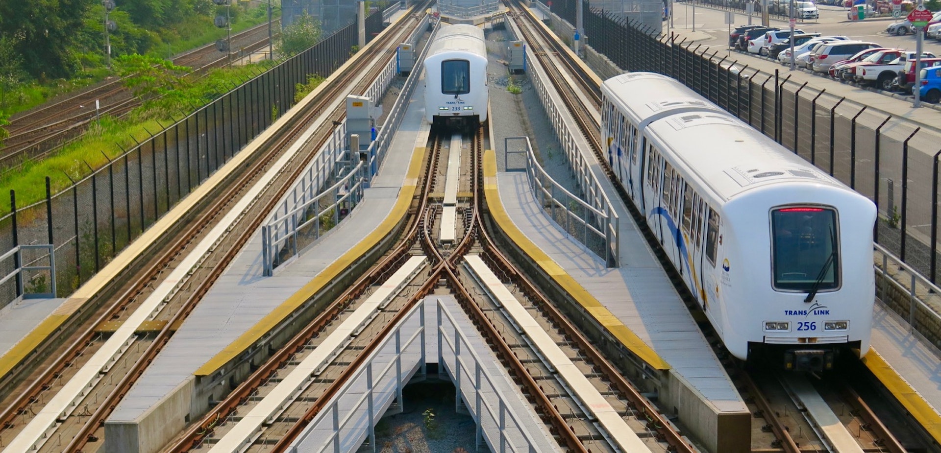 Two SkyTrain trains are on different tracks as they come out of a station