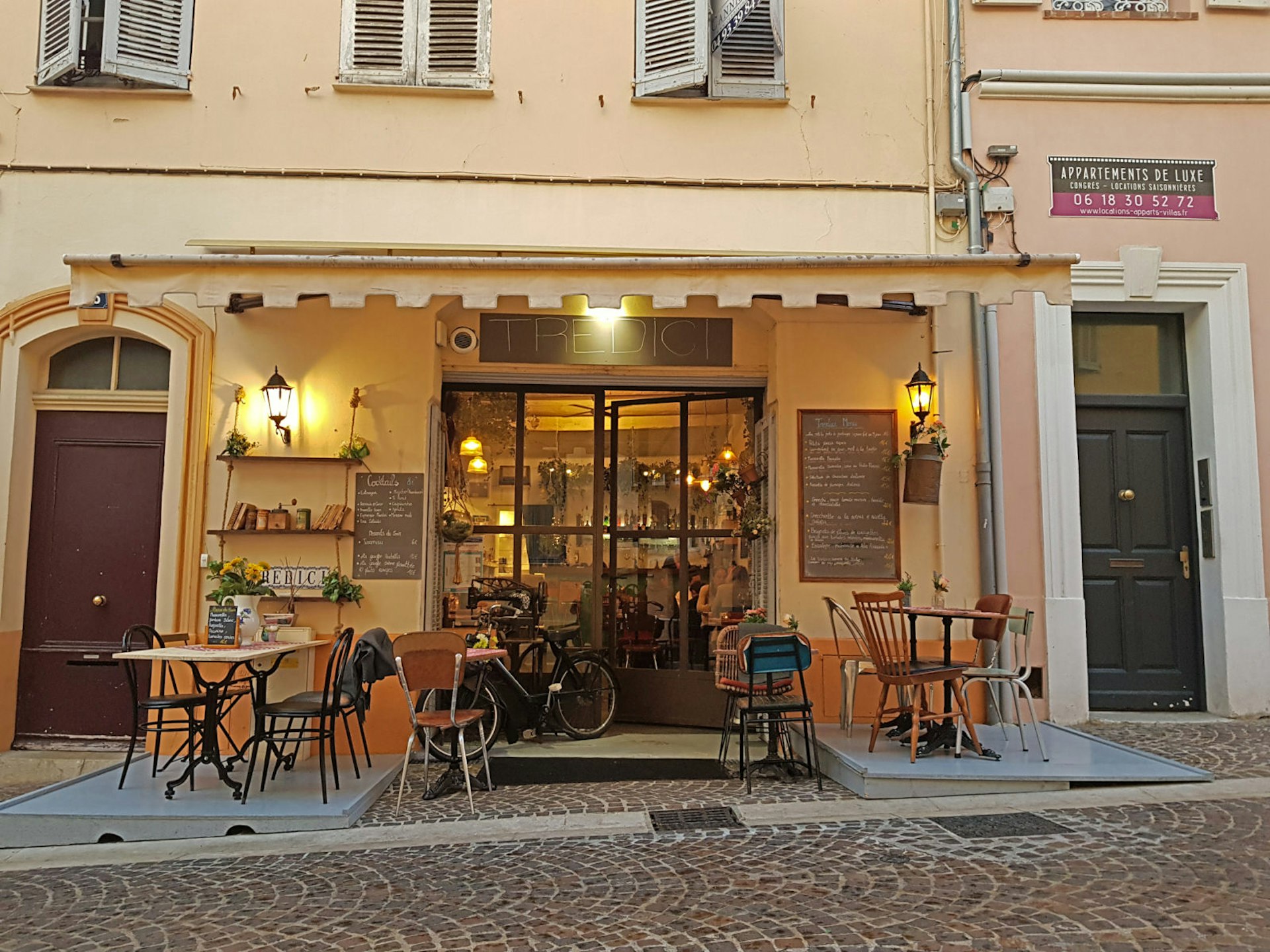 The cream shopfront of the Tredici Restaurant in Cannes with chairs outside
