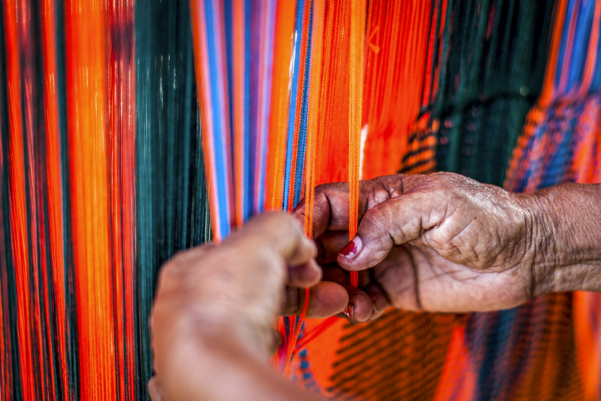 A woman weaves teal, orange, blue and purple stands to make a hammock in La Guajira, Colombia