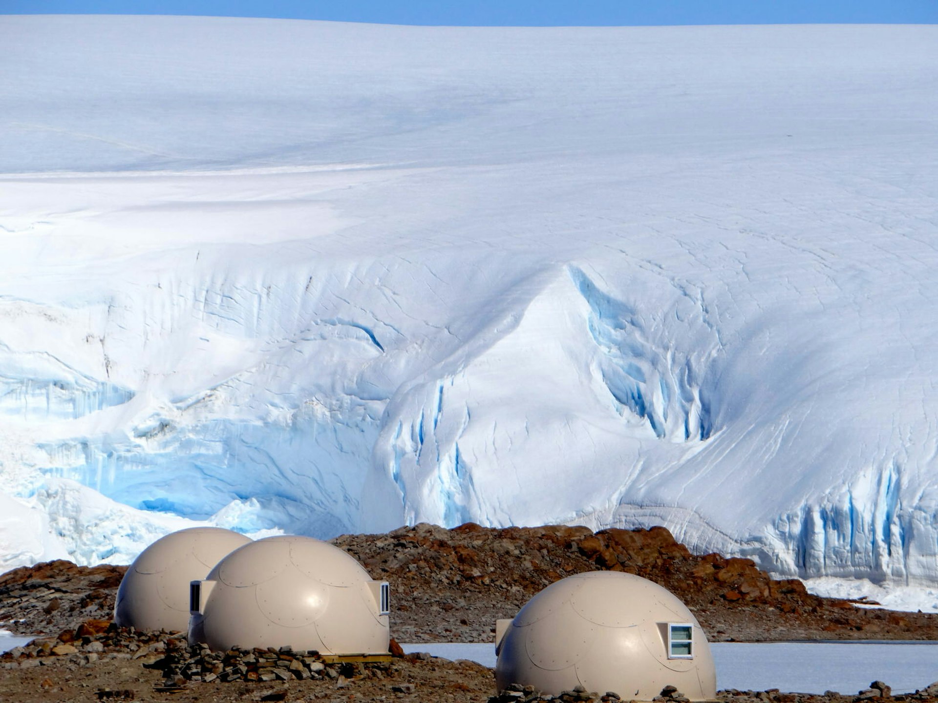 Cream-coloured domes stand in the Antarctica, with huge icebergs in the background.