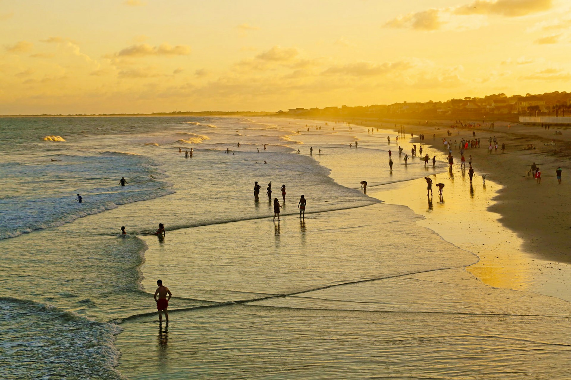 A high-angle photo of beach-goers on a long strip of sand at sunset