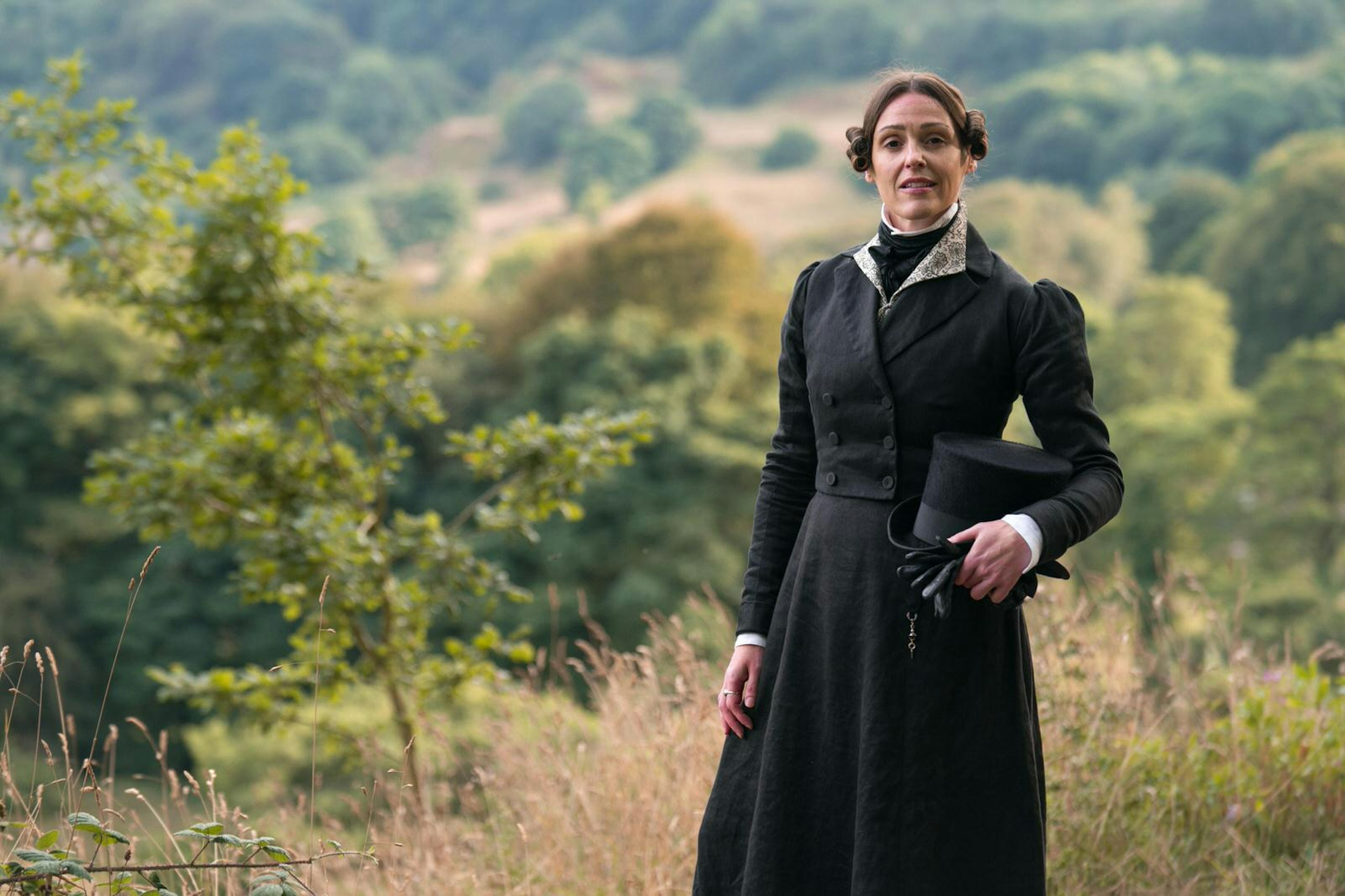 Actor Suranne Jones dressed as Anne Lister, stands holding her top hat with the Yorkshire landscape as a backdrop