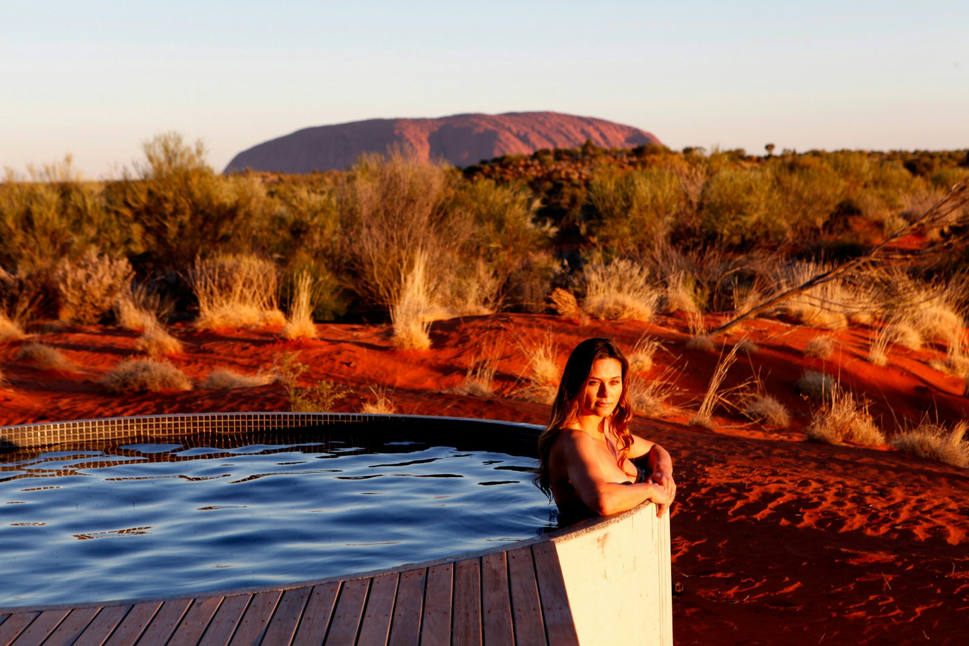 A woman sits in a hot tub with Australia's Uluru in the background.