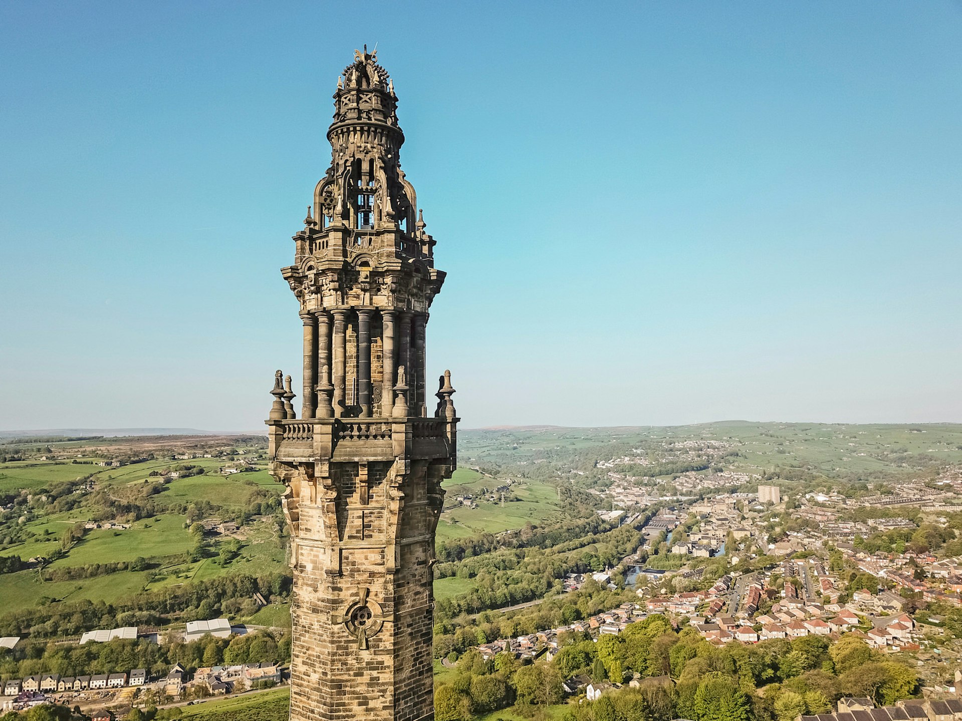Aerial view of the top of Wainhouse Tower, looking down over flat green land and the town of Halifax with red roofs