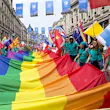 Pride in London parade participants carrying a huge rainbow flag along Regent Street; everyone is wearing matching green shirts that say 'flag bearer' on them, and unsurprisingly, they each have one hand on the rainbow flag and the other on their nation's flag (those of Sweden, Greece, China, New Zealand, Belarus are visible)