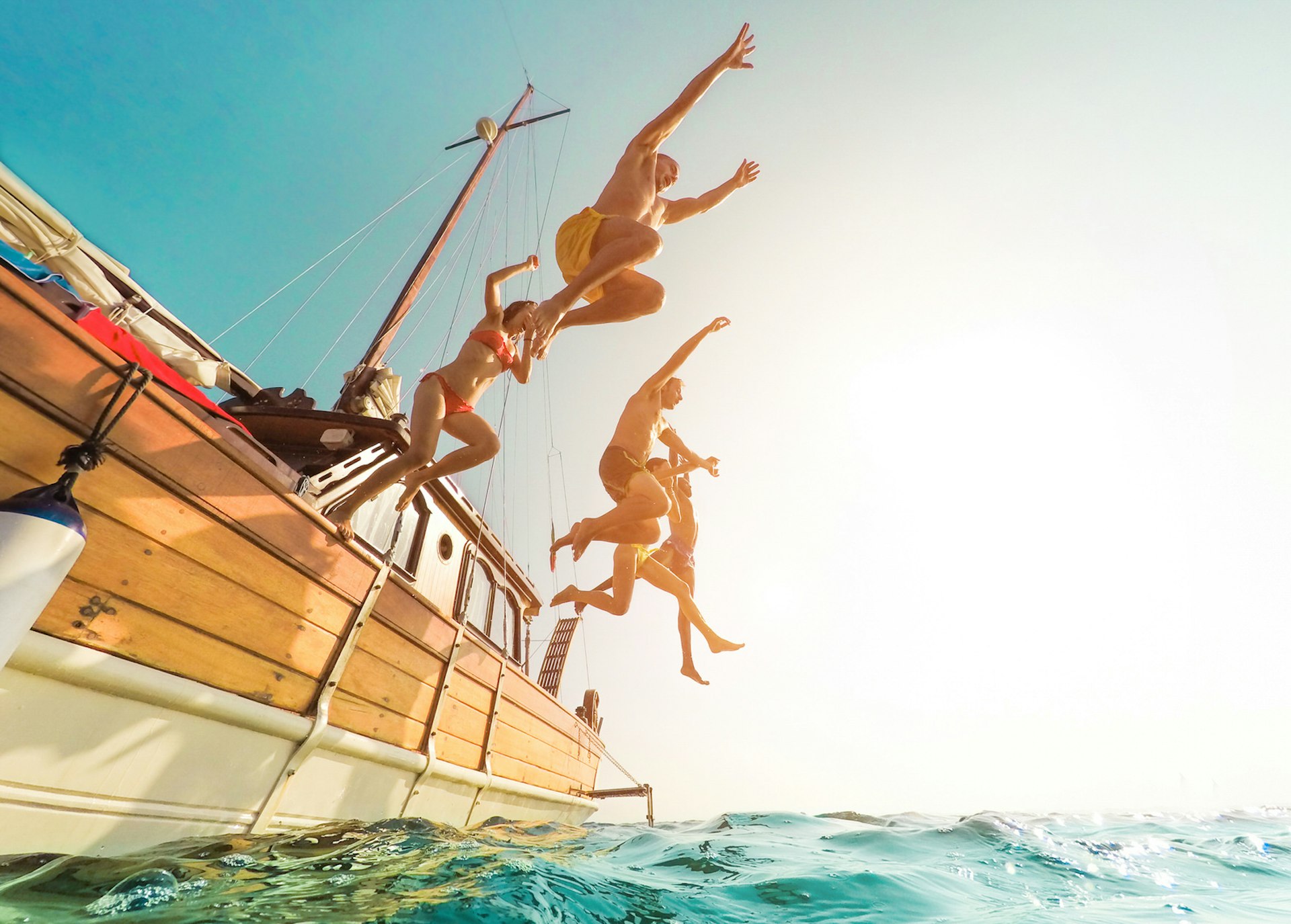 Five people jumping from a sailboat into the ocean during summer ©DisobeyArt/Getty Images