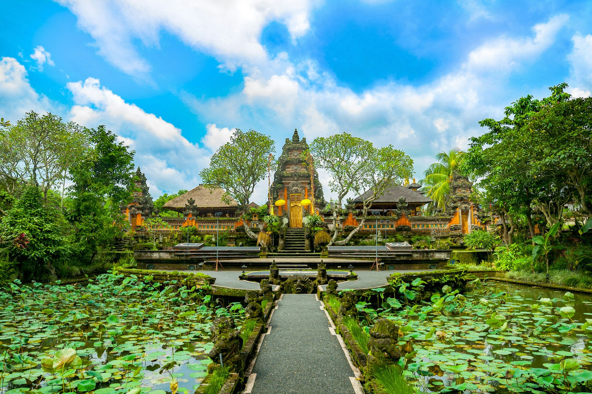 A paved path leads across a lotus covered pond in front of the temple of Pura Taman Saraswati in Ubud, Bali