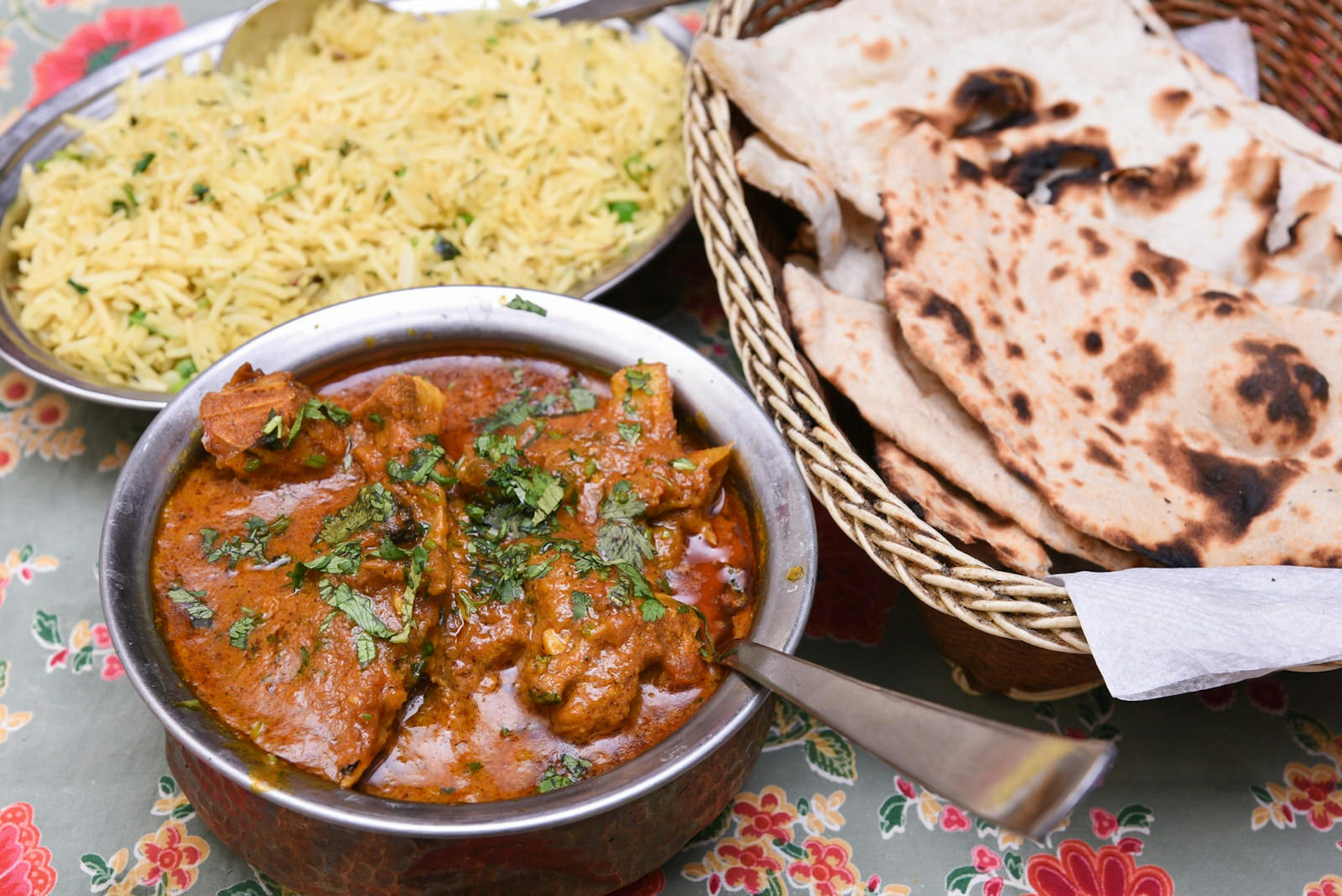 A bowl of butter chicken garnished with rice and a roti