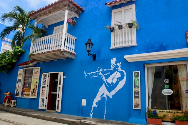 A blue wall containing a mural of a trumpet player, with a white balcony and window above; free things to do in Cartagena
