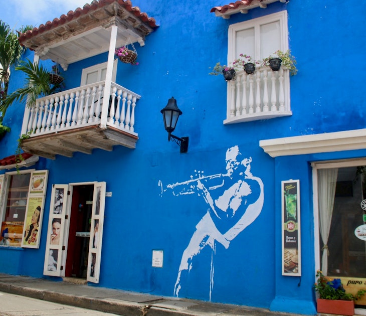 A blue wall containing a mural of a trumpet player, with a white balcony and window above; free things to do in Cartagena