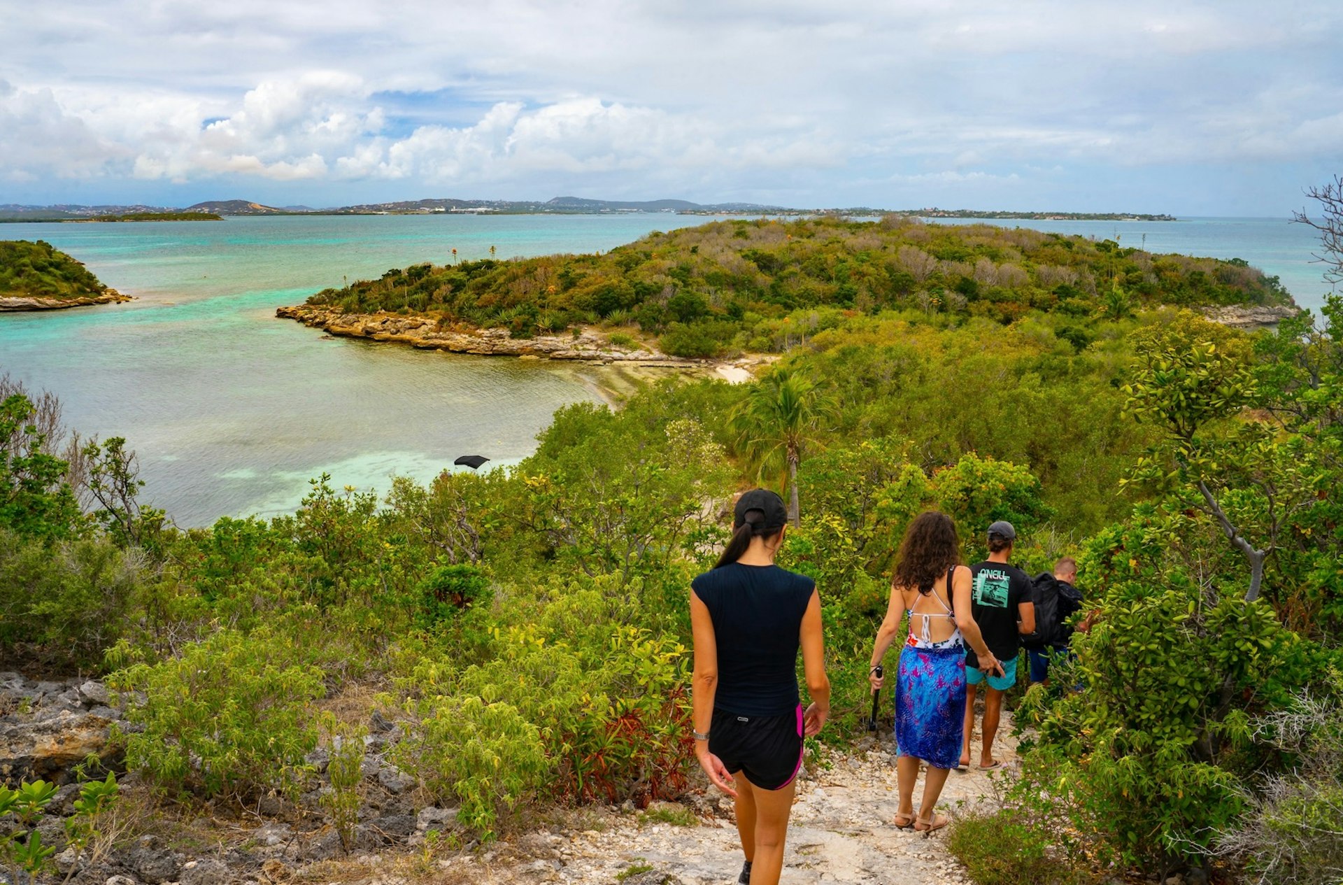 A group of people walk down a paved trail heading to Great Bird Island in Antigua and Barbuda. 