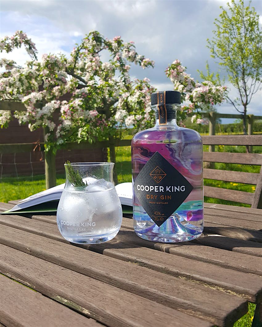 A glass full of ice sits on an outside table next to a bottle of Cooper King Dry Gin