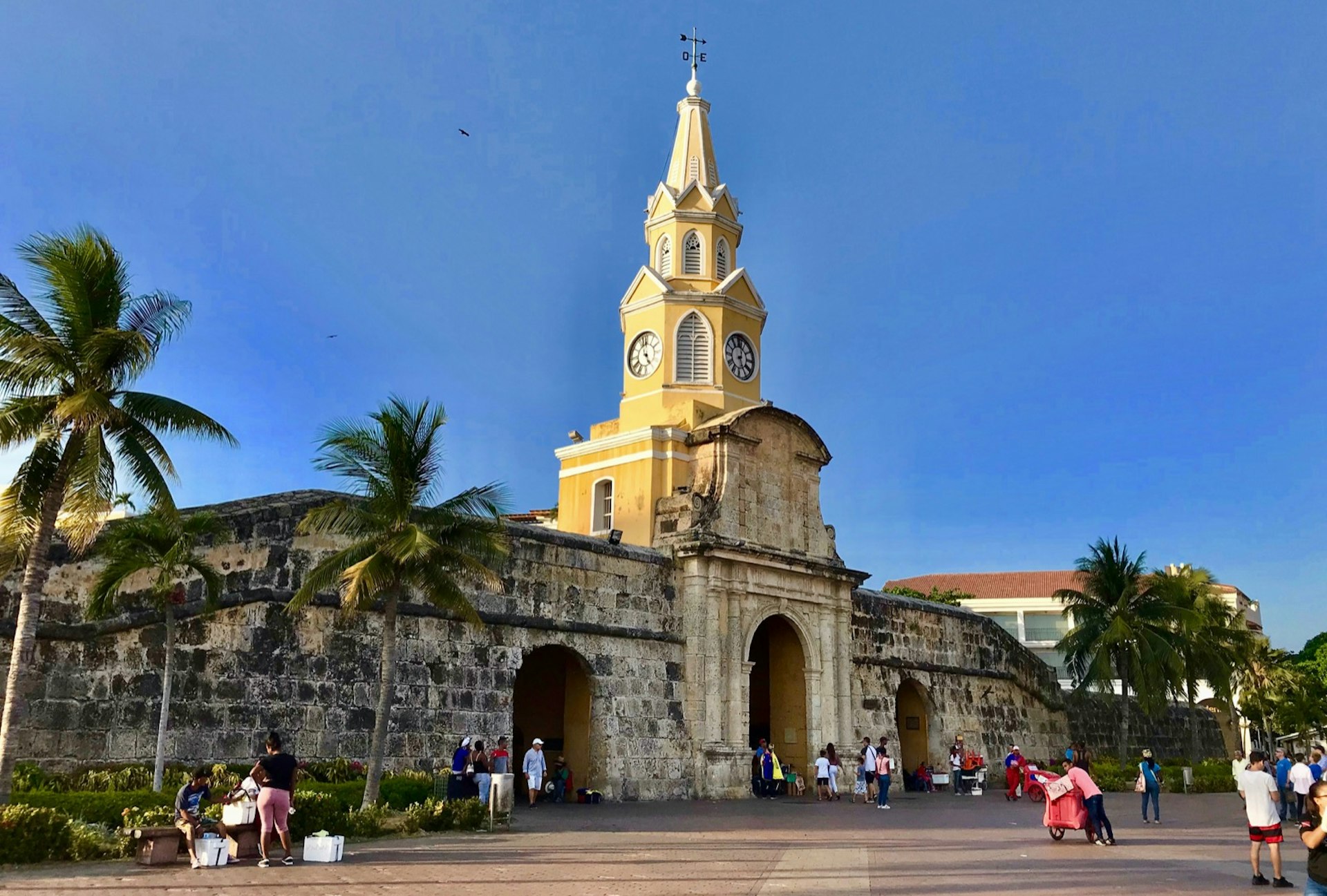 The yellow church tower over an old city wall, with people in a courtyard below; free things to do in Cartagena