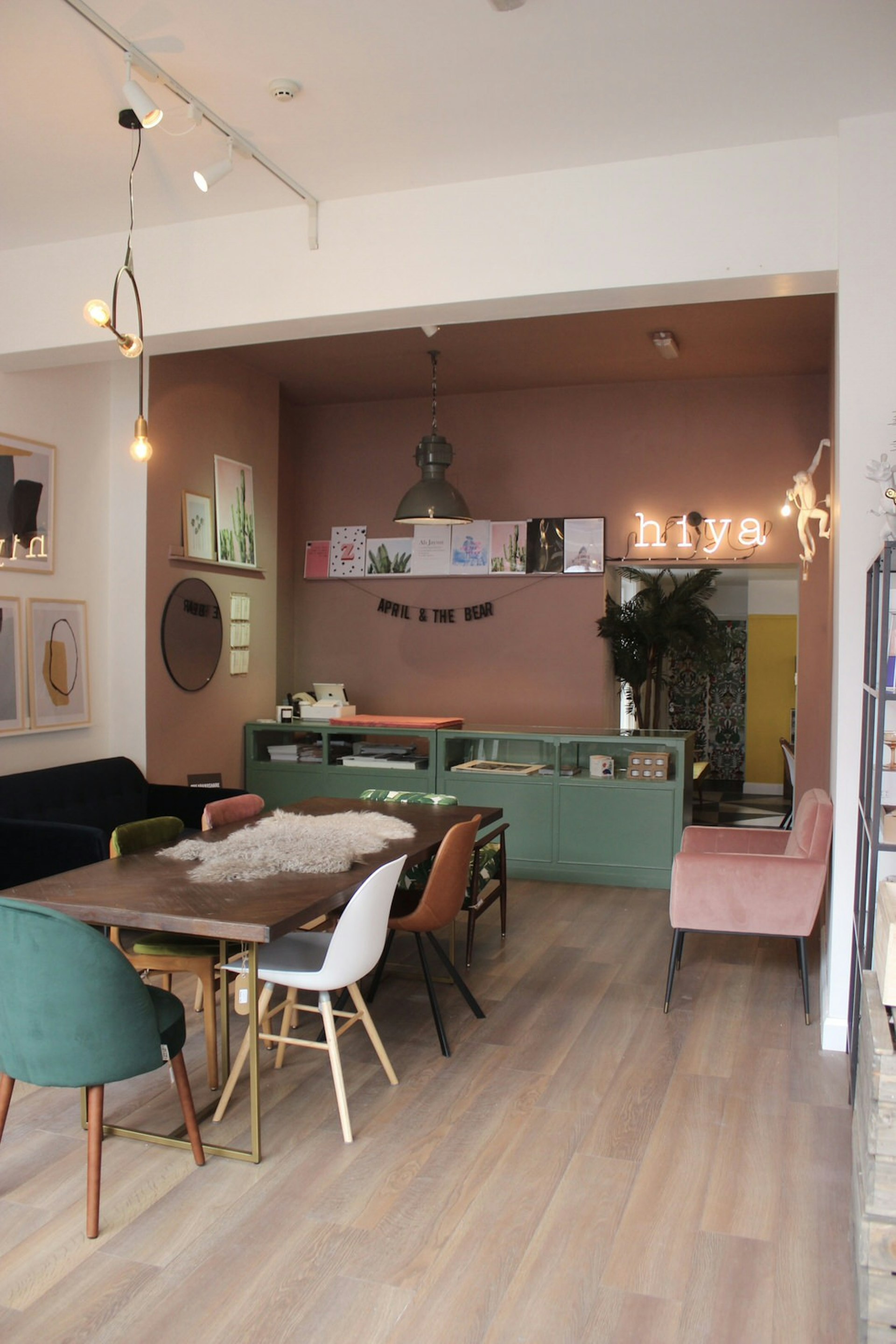 Dublin independent shops - the interior of April and the Bear independent shop with a long dark wood table in the middle surrounded by multicoloured chairs. There is a neon sign that says 'hiya' on the light-pink walls as well as other artwork and mirrors