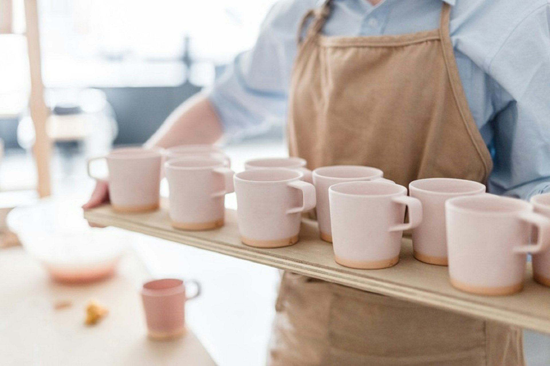Dublin independent shops - a long wooden tray of light-pink clay mugs being carried by someone in a blue shirt and brown apron whose head's been cropped out