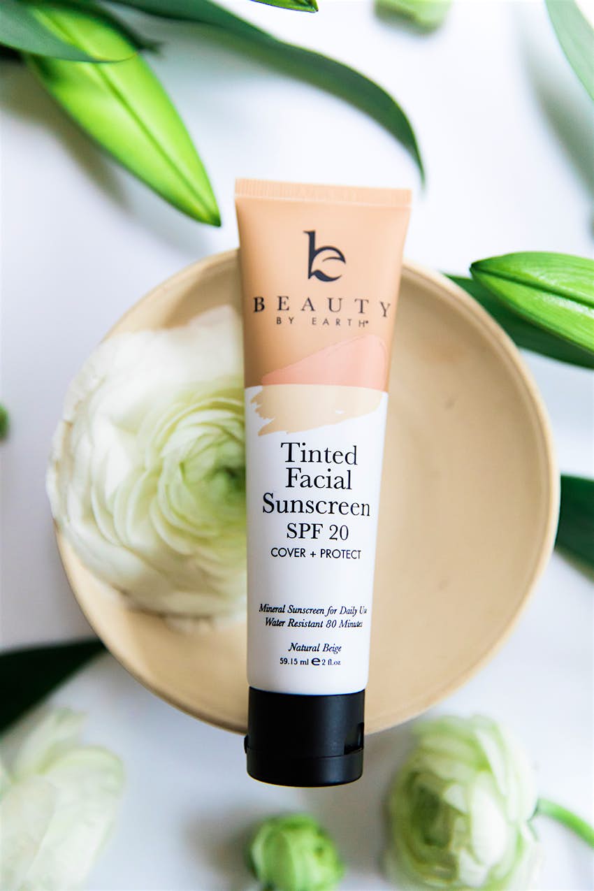 Features - Beauty By Earth A tube of facial sunscreen sitting on a bowl with a flower in it.