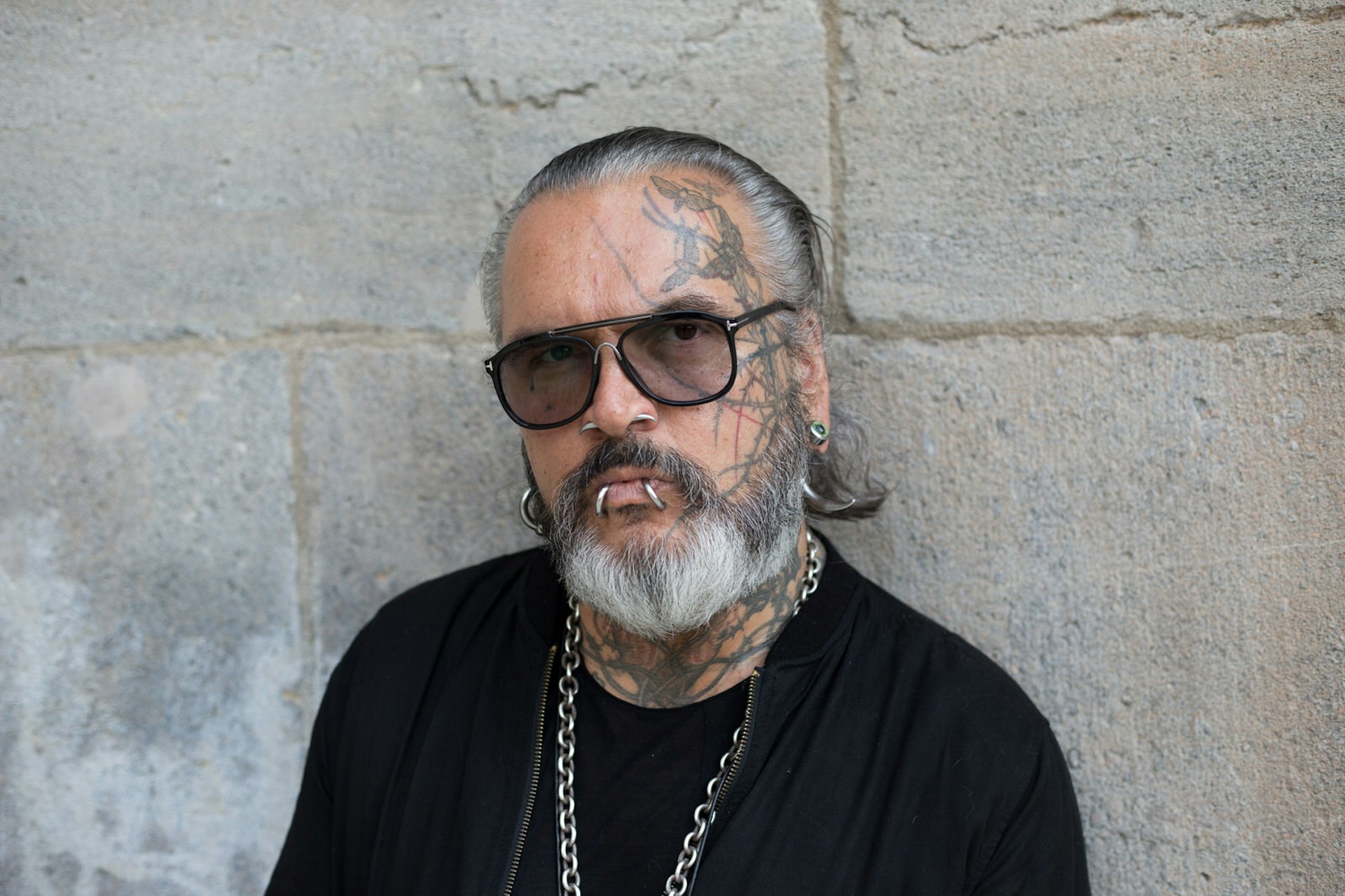 Berlin clubs - Berghain doorman Sven Marquardt poses at Volksbuehne theater in Berlin, Germany. Sven is a legendary and feared doorman with facial tattoos and piercings. He wears dark sunglasses, a black t-shirt, a heavy silver chain. He has a grey beard and slicked-back grey hair