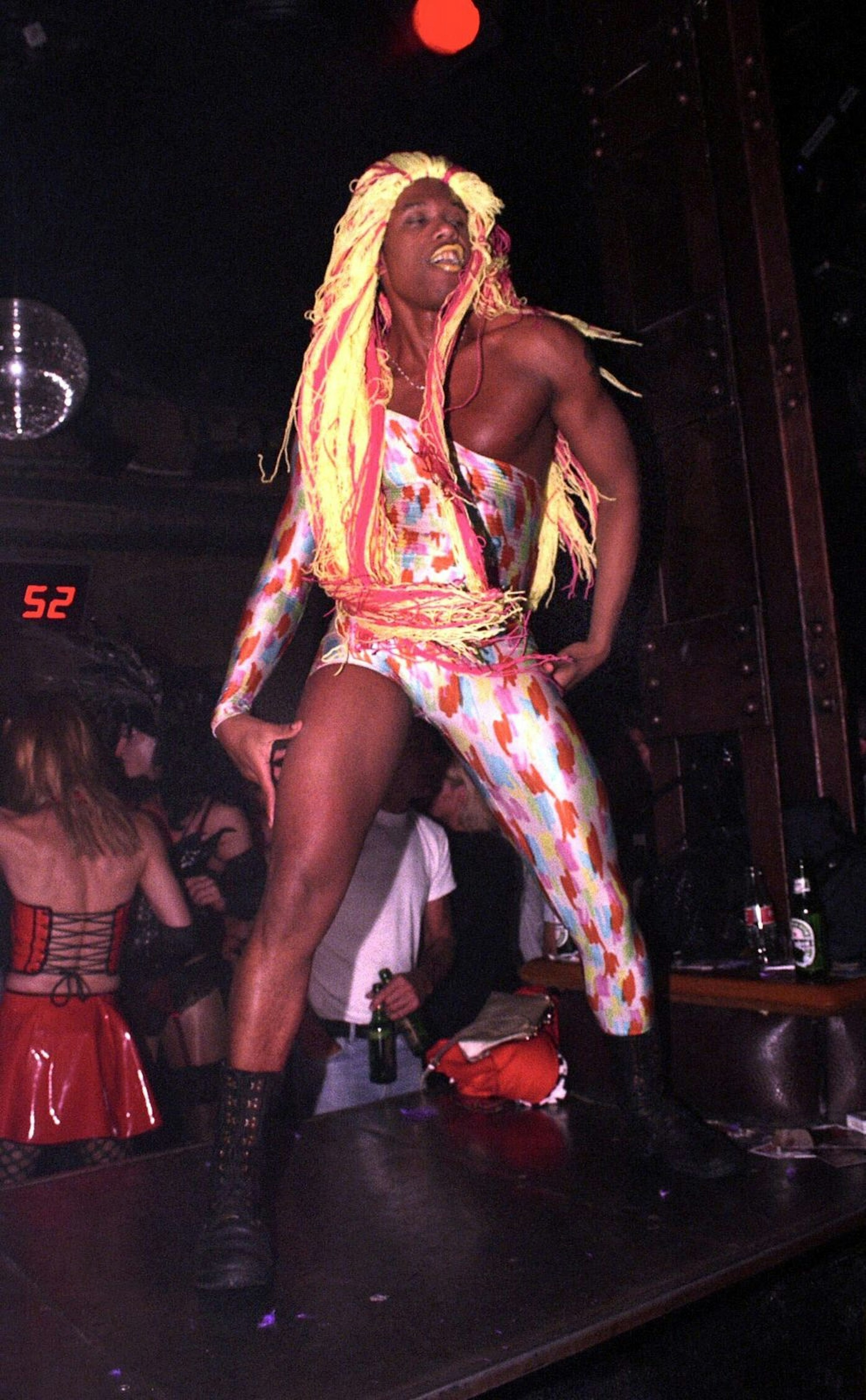 Berlin clubs - a Sage Club gogo dancer dances on stage wearing a multi-coloured leotard with one arm and one leg as well as a blonde wig with pink streaks