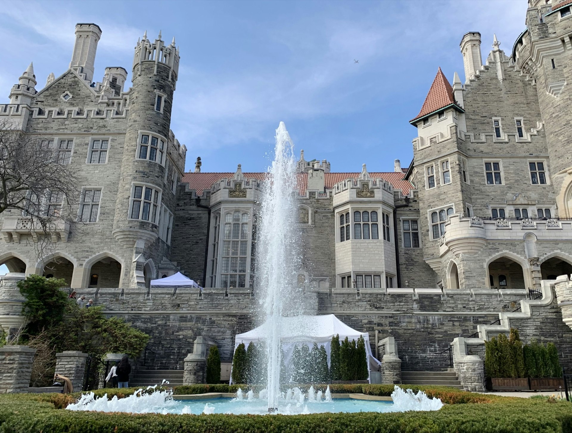 A very tall fountain is seen outside of the stone, castle-like facade of Casa Loma in Toronto