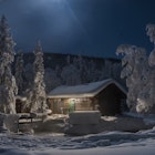 A snow-covered cabin and trees surround a water hole at night at Chena hot springs near Fairbanks Alaska.