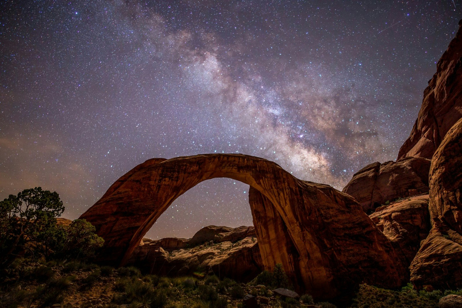The Milky Way is seen in a dark sky above the stone arch of Rainbow Bridge National Monument