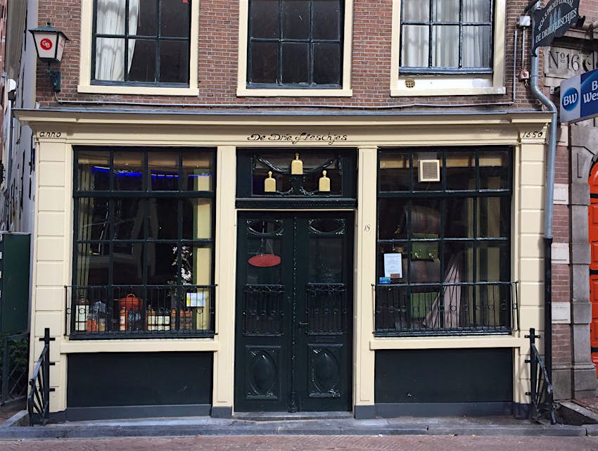 An old brick building with wooden-framed windows (painted dark green) on a cobbled street in Amsterdam; it's one of the best places to sip jenenver in Amsterdam