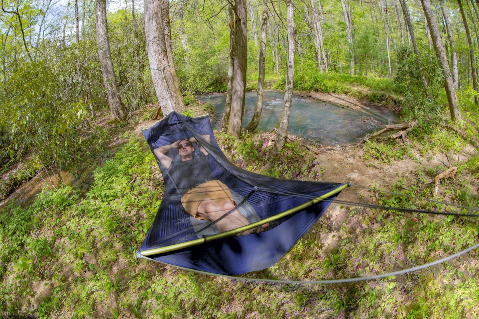 a man lounges in a flat hammock covered with a bug net