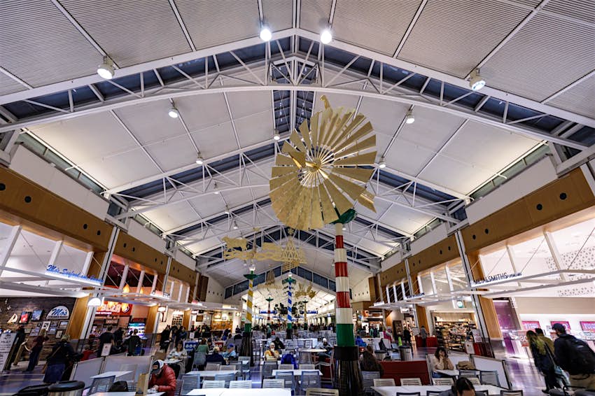 Customers dine at the food court at Portland, International Airport - PDX . There's a large hanging sculpture that resembles a windmill hanging from the high ceiling and lots of natural light
