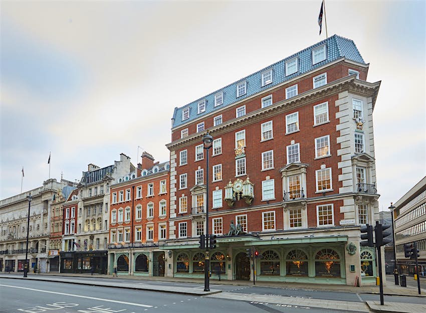 A seven story red-brick building, with white wooden window frames, rises above Picadilly road; the ground floor has elaborate arched wooden frames around all its windows and the door, which is painted a pale green colour in line with Fortnum & Mason