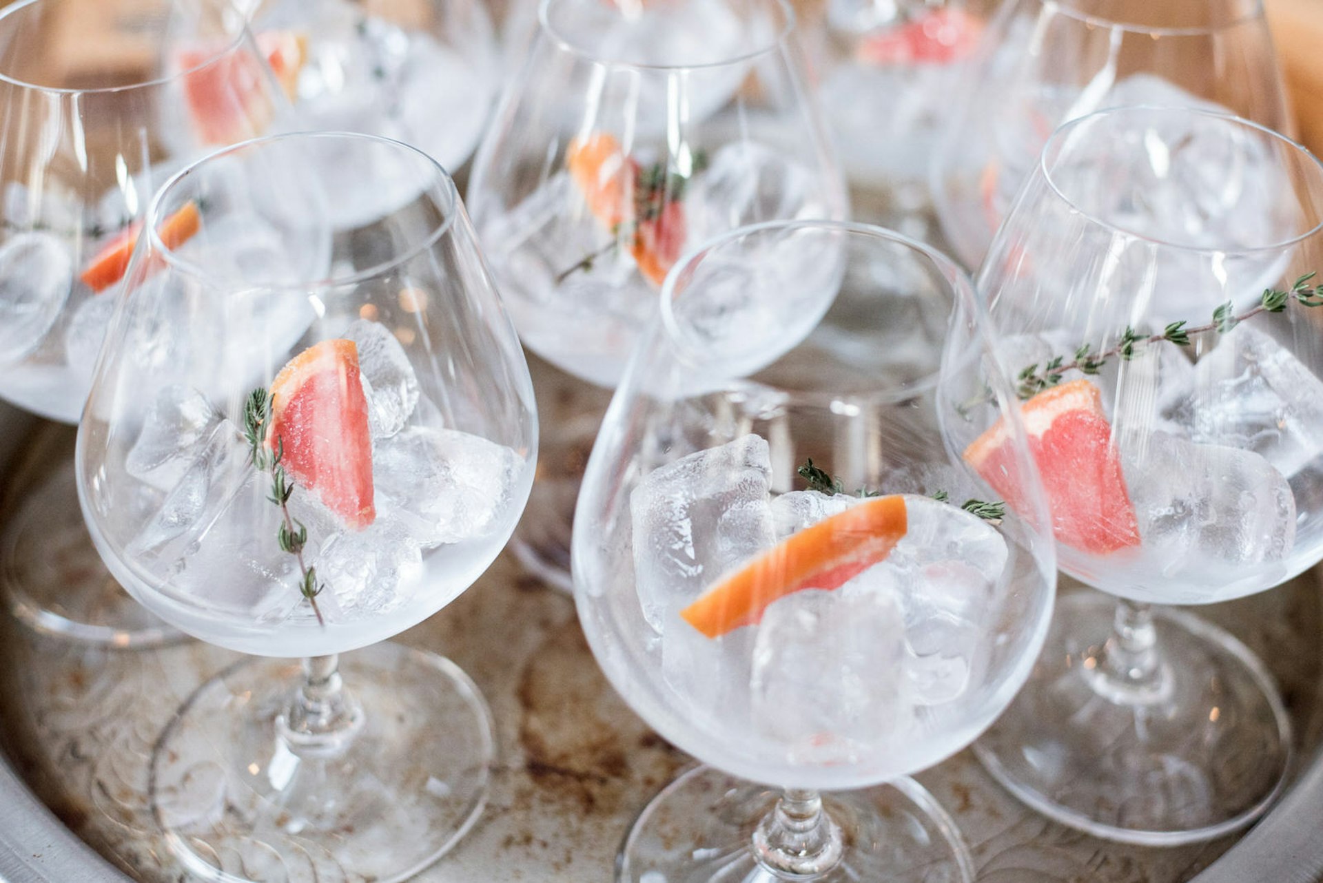 Cape Town gin - An aged silver tray filled with short wine-like glasses, each containing ice, a sprig of rosemary, a tiny wedge of pink grapefruit and gin
