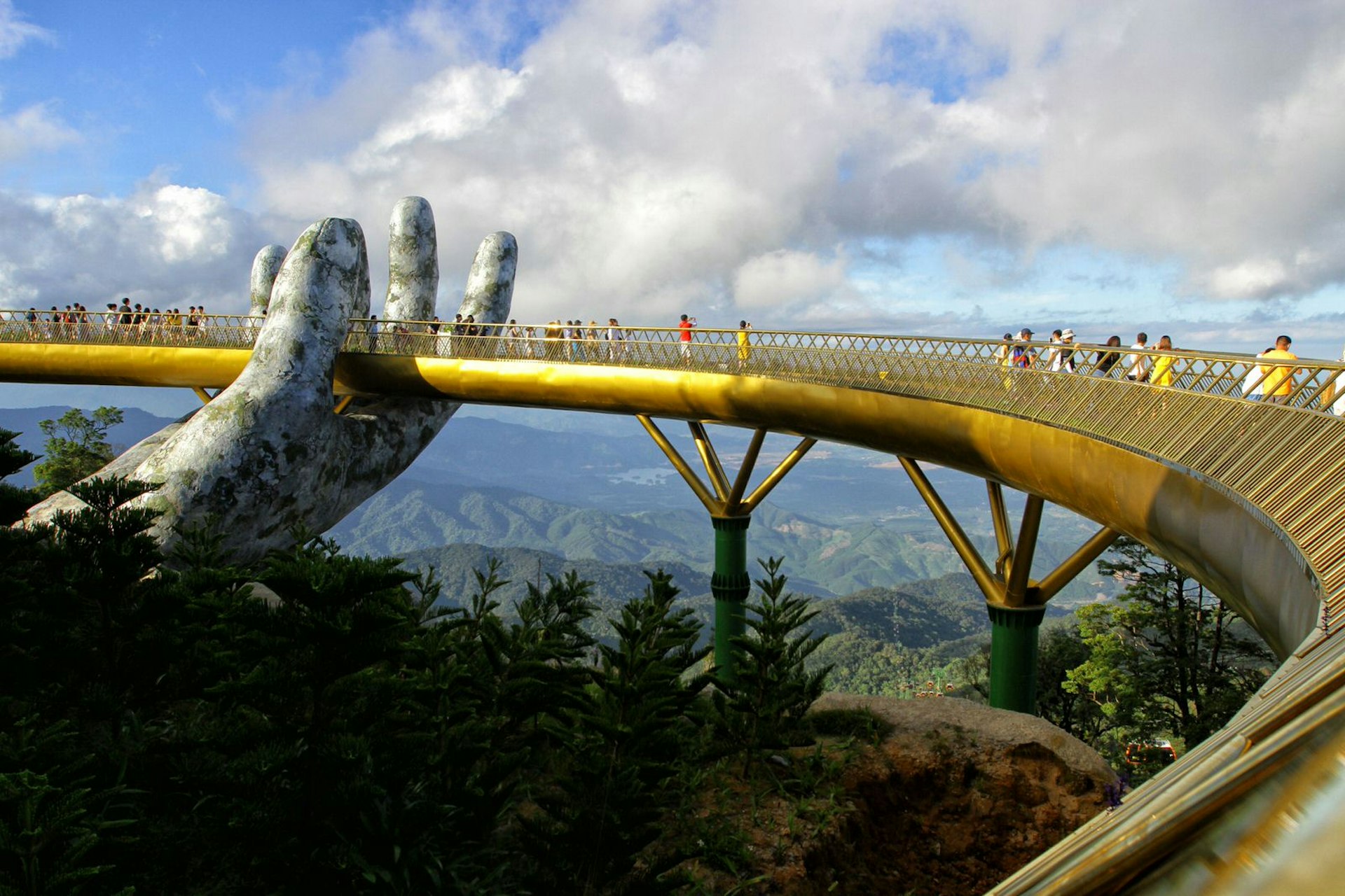 One giant concrete hand can be seen holding the golden walkway of the bridge, as several people enjoy the view of jungle and hills that stretches for miles